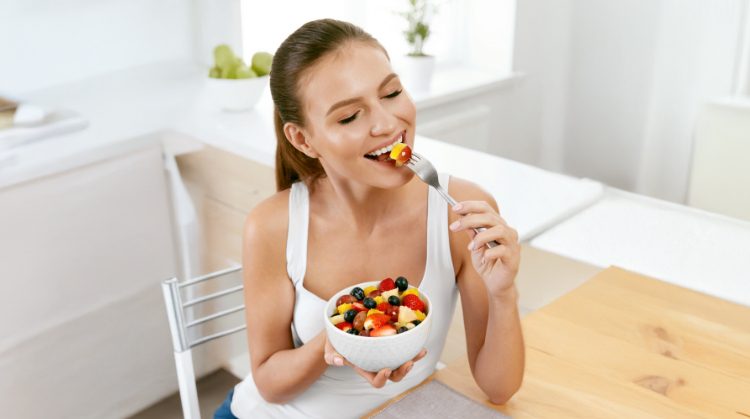 Smiling woman enjoying a fresh fruit salad, highlighting healthy eating tips for maintaining oral health during the holidays in Glendale, AZ.