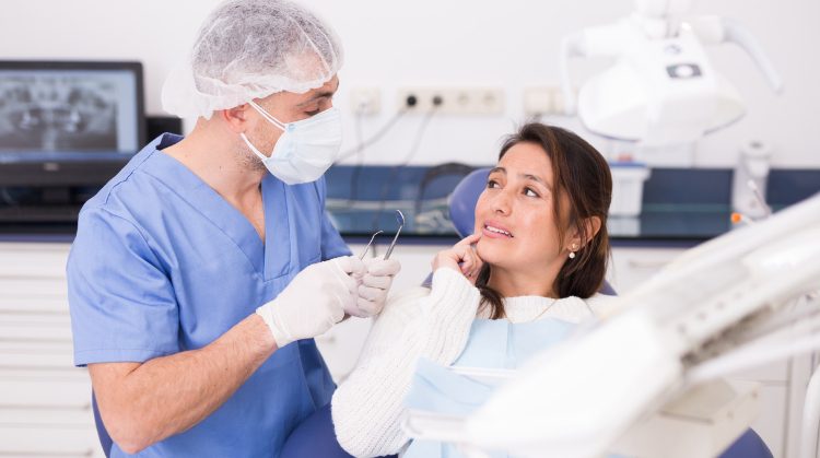 Patient holding her cheek in pain while a dentist examines her in a dental clinic, suggesting a dental emergency situation.