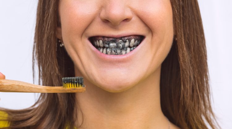 Woman brushing teeth with charcoal toothpaste, showing black-stained smile – Palo Verde Smiles, Glendale, AZ.